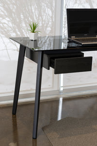 Close up of smoke glass desk with metal legs and black side drawer.