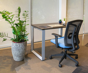 Side view of loop leg desk with a laptop and notebook on the surface. A grey and blue office chair is in front of the desk.