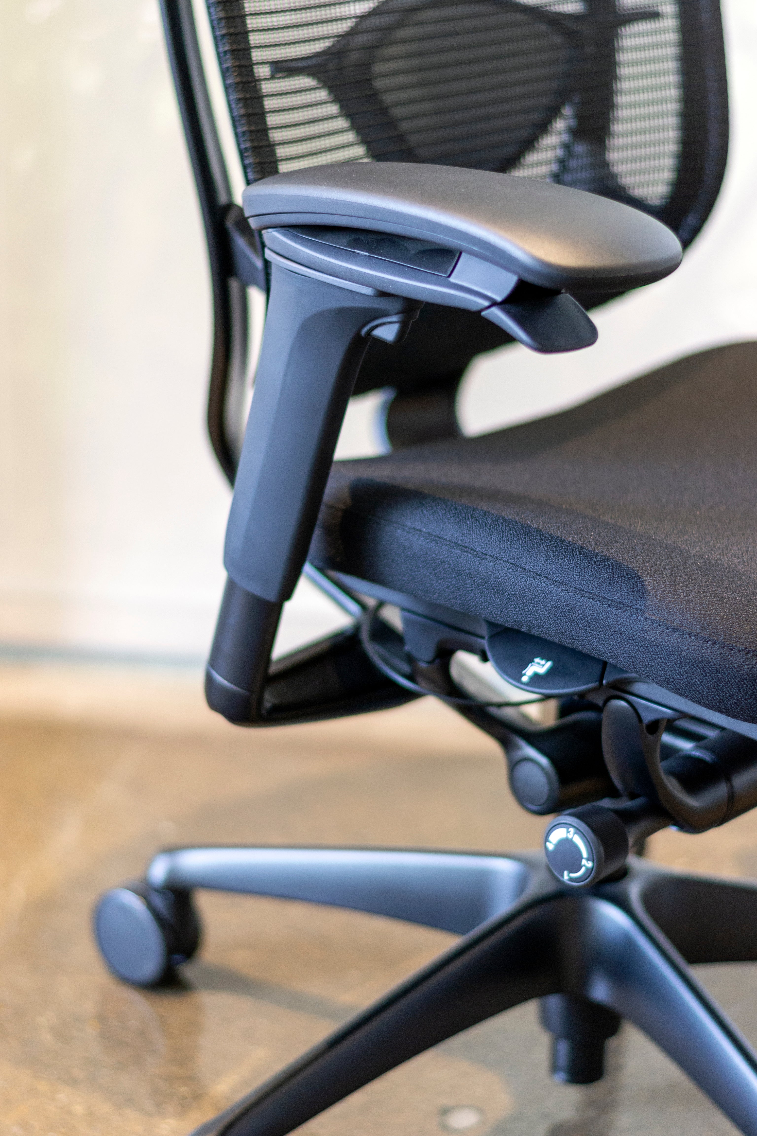 Close up side view of black Nuova work chair showing multiple adjustment levers located on arm rests on seat pan.