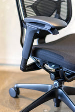 Load image into Gallery viewer, Close up side view of black Nuova work chair showing multiple adjustment levers located on arm rests on seat pan.
