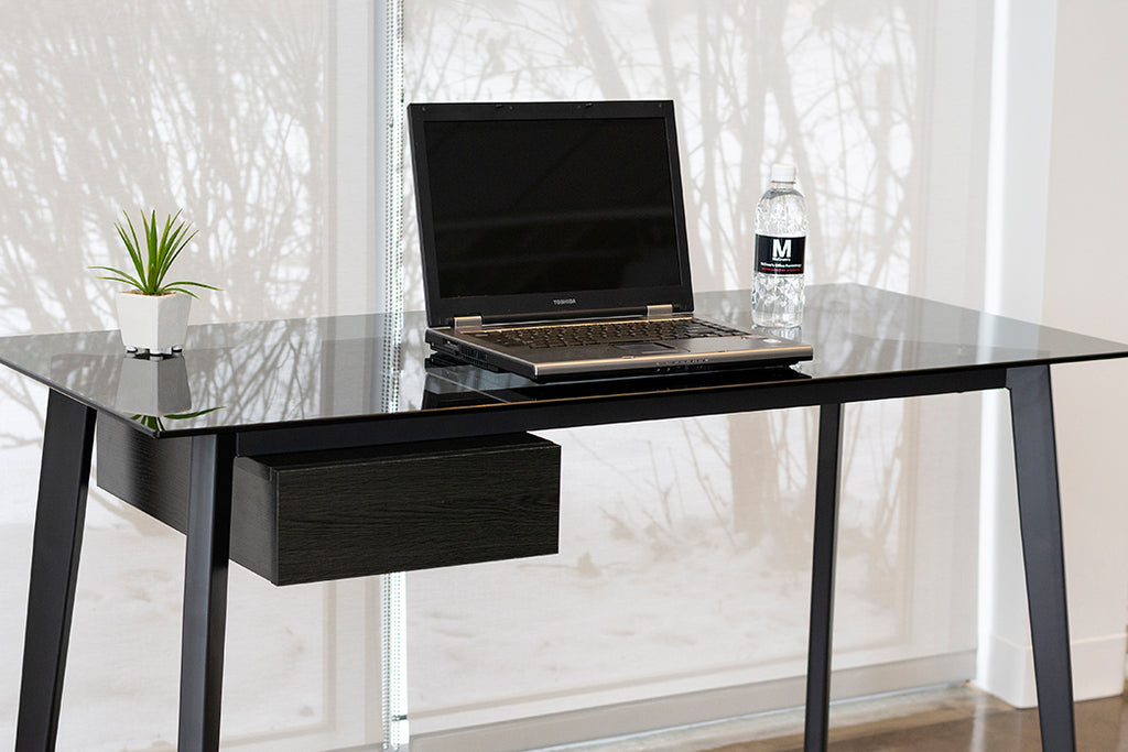 Smoke glass top desk with metal legs and small black side drawer. Laptop on surface.